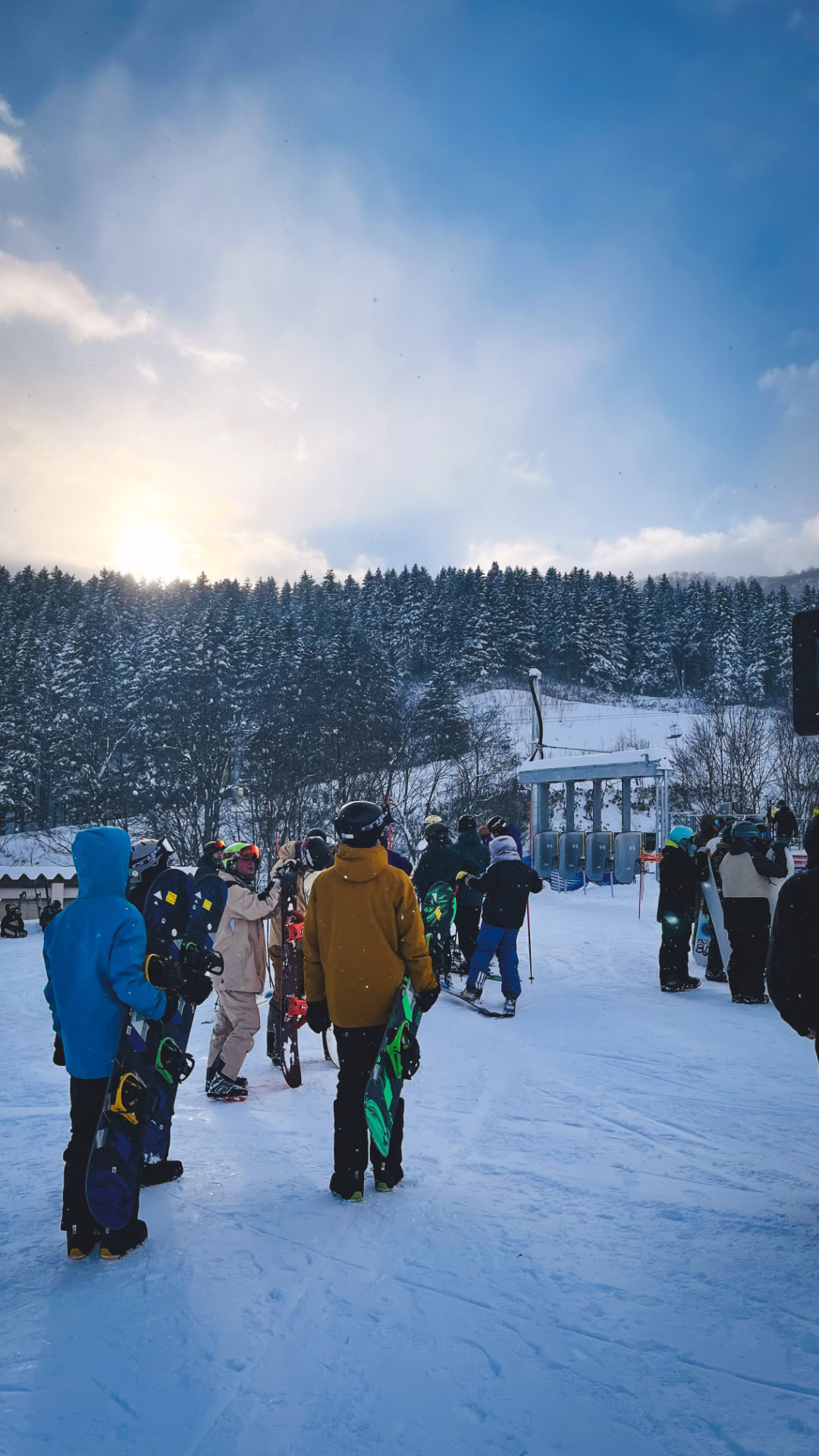 Snowboarders and skiers at the base of a mountain at sunset